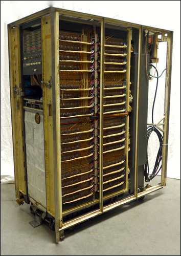 A large cabinet with its exterior panels removed, holding many layers of vertically oriented
                    thin cards, each one holding a fragment of core memory.