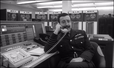 A still image of Peter Sellers from the film Dr. Strangelove. Sellers is sitting at a
                        computer console talking on a multiline dial telephone.